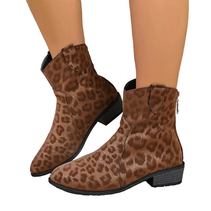 A pair of brown ankle boots with a leopard print pattern, shown on a model's feet with a brown hat and a beige textured background.