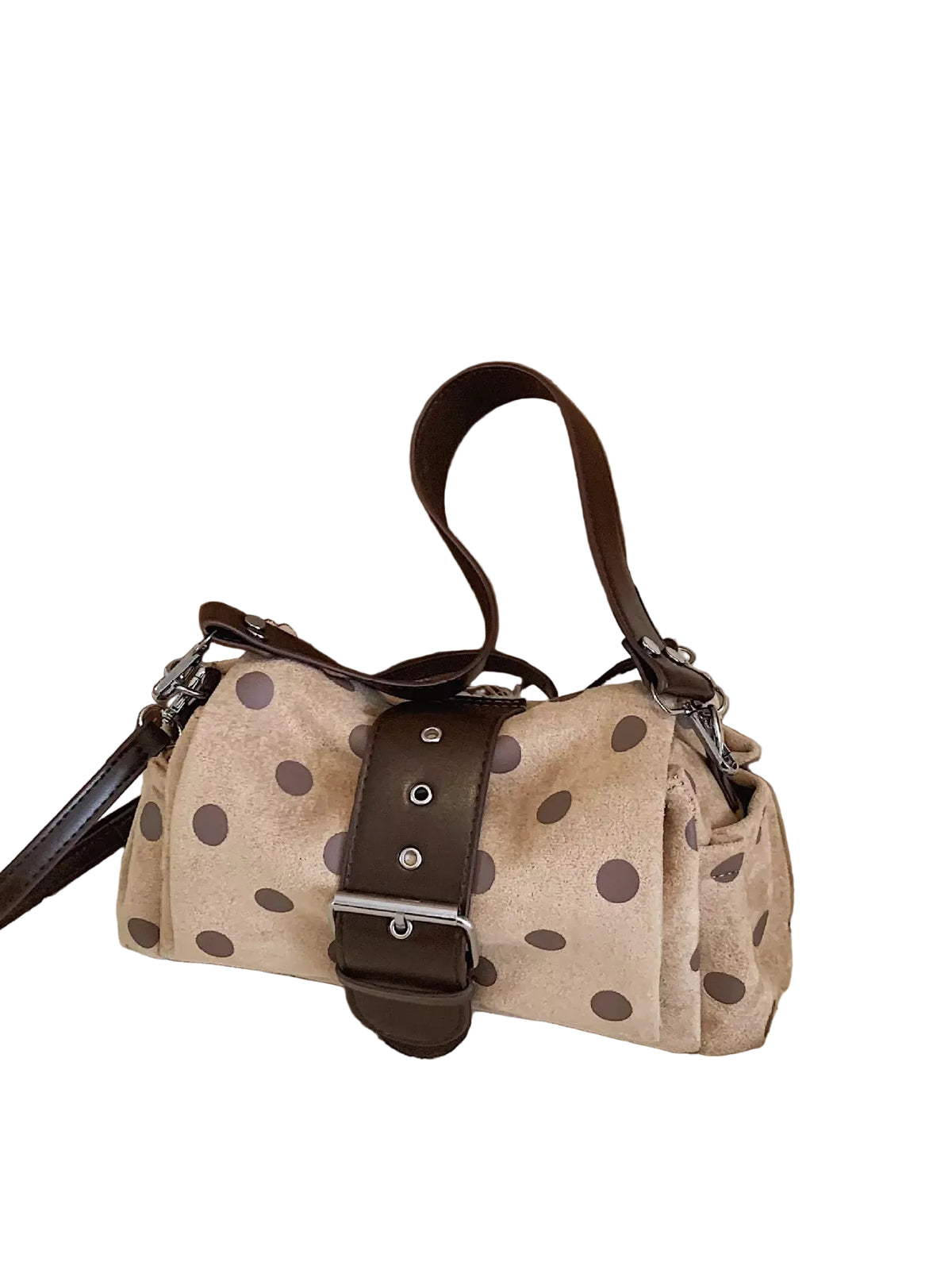 A beige shoulder bag with dark brown polka dots and a dark brown leather strap closure, resting on a textured beige rug next to a white dust bag and a wooden wall.