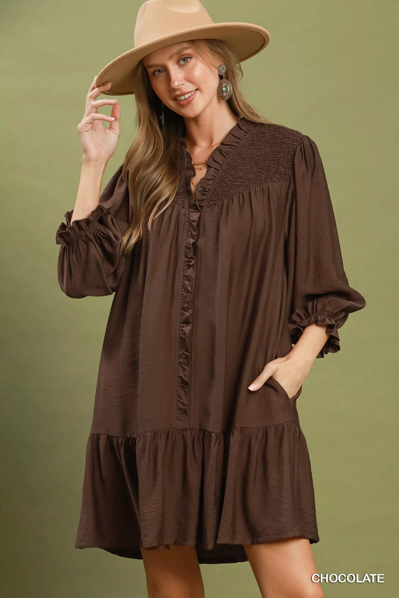 Woman wearing a brown dress and beige hat against a green background