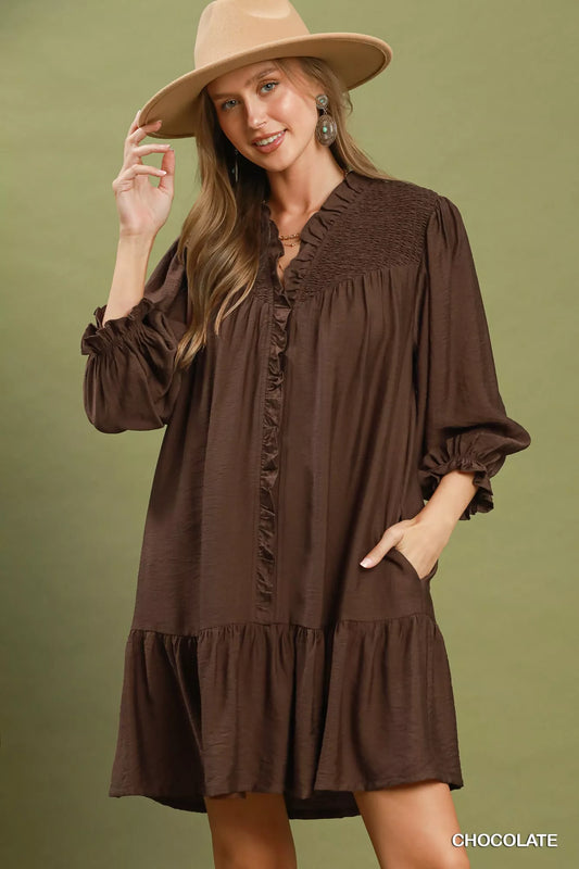 Woman wearing a brown dress and beige hat against a green background