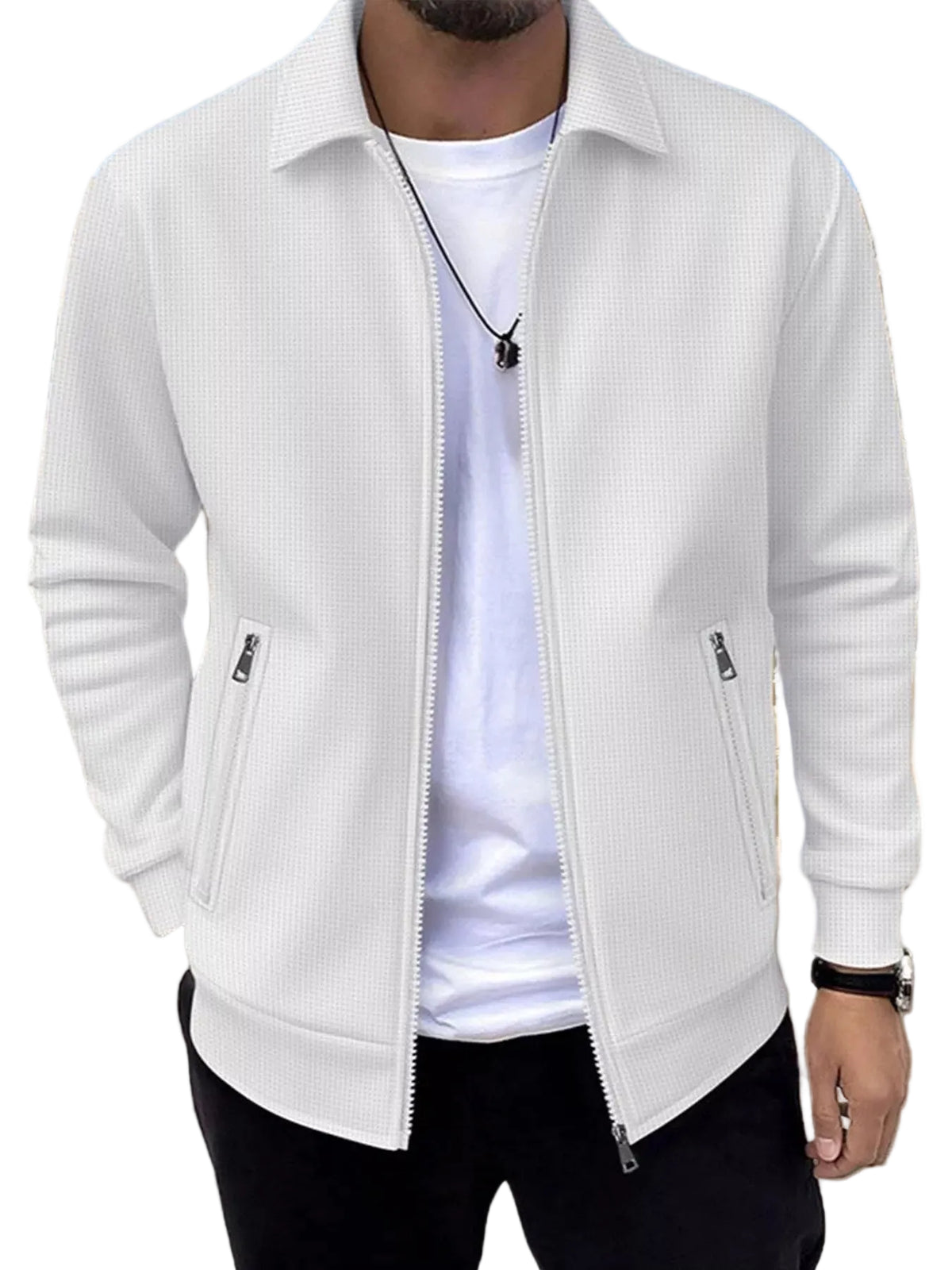 A man wearing a white textured zip-up jacket over a white t-shirt and black pants, standing outdoors in front of a building with a blue sky background.