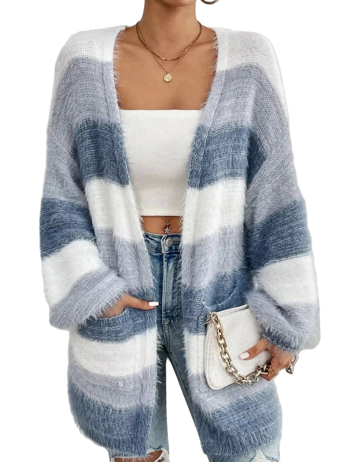 A woman wearing a fuzzy open-front cardigan with wide horizontal stripes in light blue, medium blue, and white, styled over a white crop top and blue jeans, holding a small white handbag.