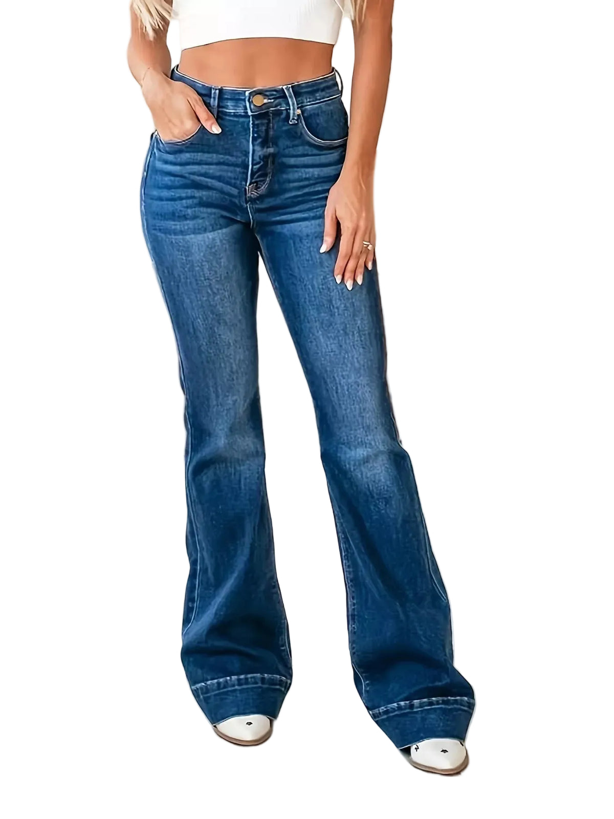 A person wearing high-waisted blue flare jeans with a straight-to-flared leg, standing in a bright living room with a beige sofa and white table visible in the background.