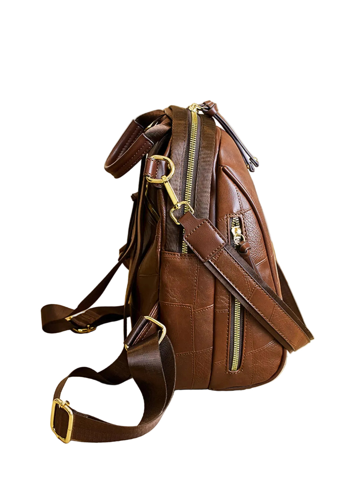 A brown leather crossbody backpack with gold-tone hardware, displayed on a light wood table in a modern interior setting.