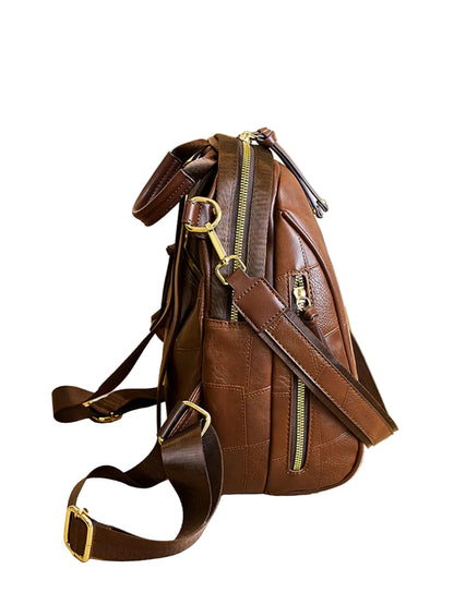 A brown leather crossbody backpack with gold-tone hardware, displayed on a light wood table in a modern interior setting.