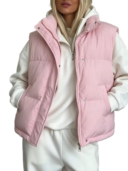 A woman wearing a light pink puffer vest over a white zip-up hoodie and white sweatpants, shown from the lips down in an indoor setting.
