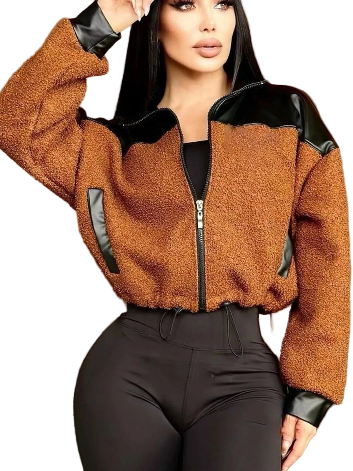 A woman wearing a cropped brown sherpa jacket with black faux-leather trim and black high-waisted pants, posed against a warm brown studio background.