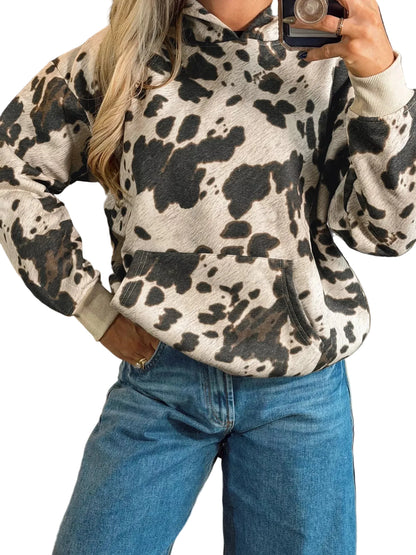 A person wearing a cow-print hoodie with a beige base and dark brown spots, paired with blue jeans, taking a mirror selfie in what appears to be a boutique setting.