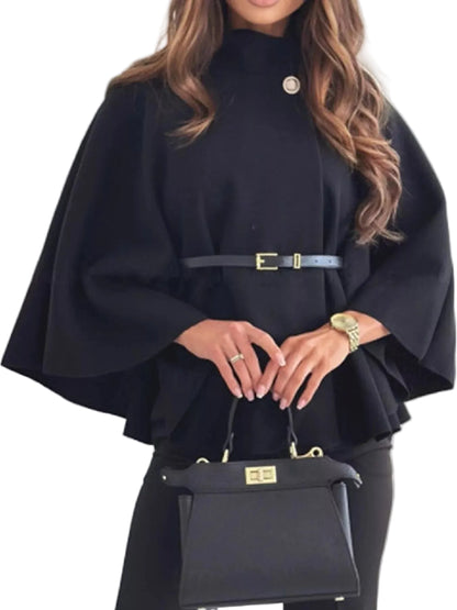 A woman wearing a black high-neck cape-style top with a thin belt at the waist, holding a structured black handbag with gold hardware.