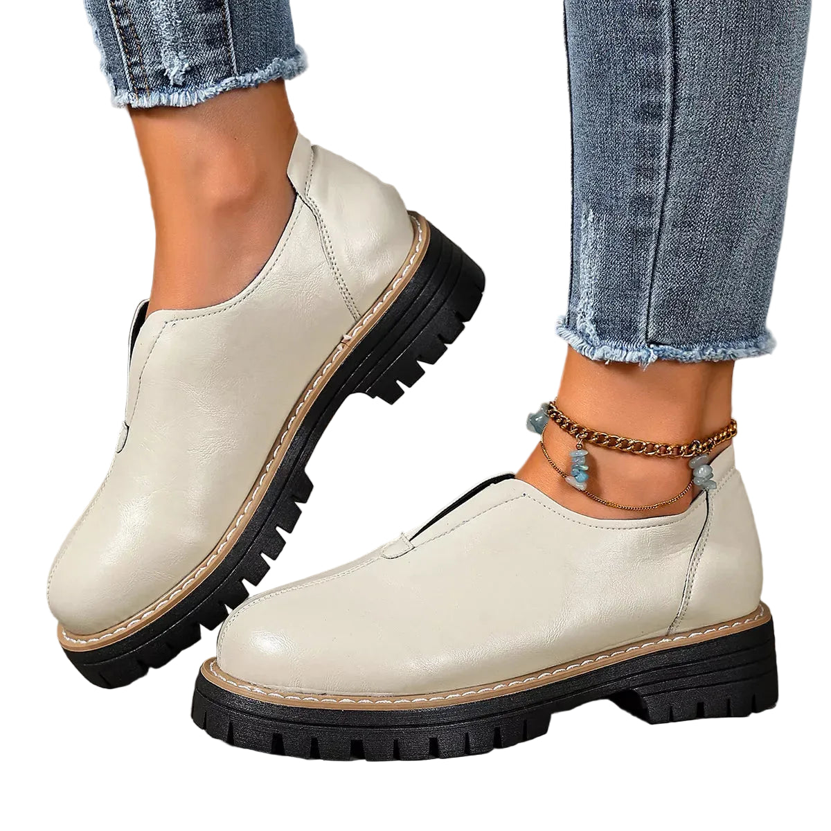 A pair of women's off-white leather oxford-style shoes with chunky black lug soles, shown on a model wearing blue jeans in a rustic outdoor setting.