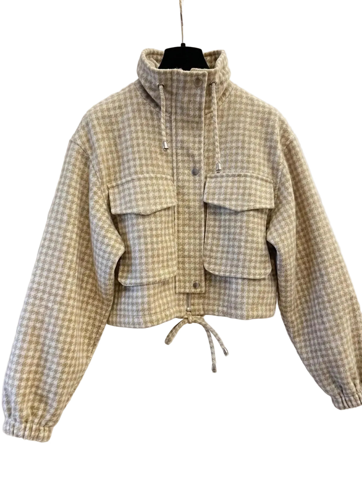 A beige and white gingham cropped jacket with a mock neck, drawstring hood, and front flap pockets, hanging on a black hanger against a white paneled door background.