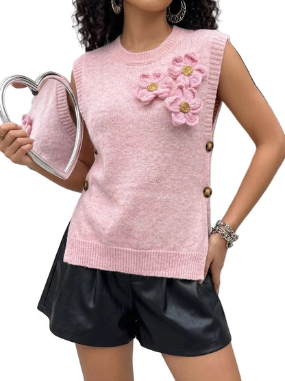 A woman wearing a light pink sleeveless knit sweater vest with 3D crocheted flowers on the chest and brown buttons on the side, paired with black faux leather shorts. She is holding a heart-shaped hand mirror.