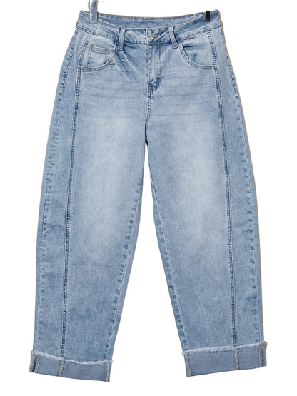 Light wash blue denim jeans with a cuffed ankle and raw hem, hanging against a plain beige background.