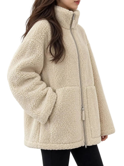 A woman wearing a cream-colored sherpa fleece jacket with a high collar and front zipper, paired with black pants, against a plain white background.