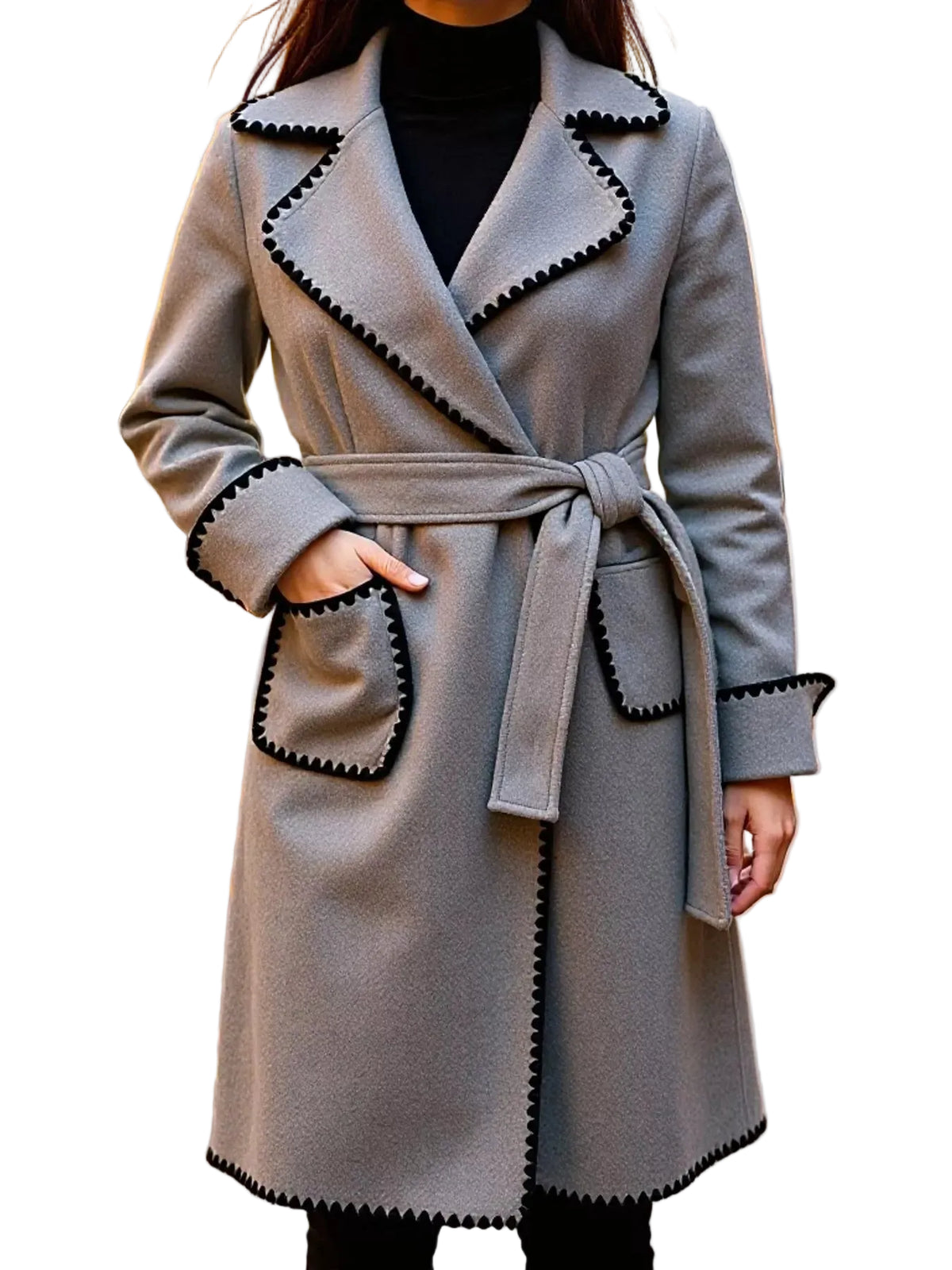 A woman wearing a light gray belted coat with black scalloped trim, photographed outdoors on a street with fallen leaves and blurred buildings in the background.