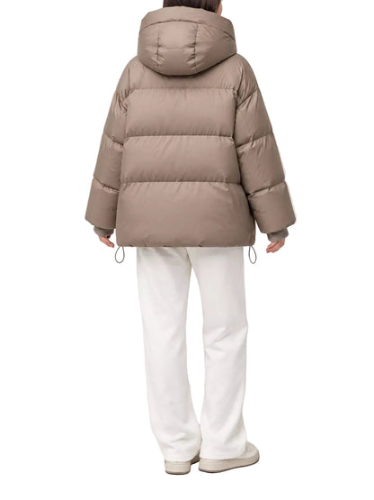 A person shown from the back wearing a taupe-brown puffer jacket with white pants and light-colored shoes, photographed against a plain light gray studio background.