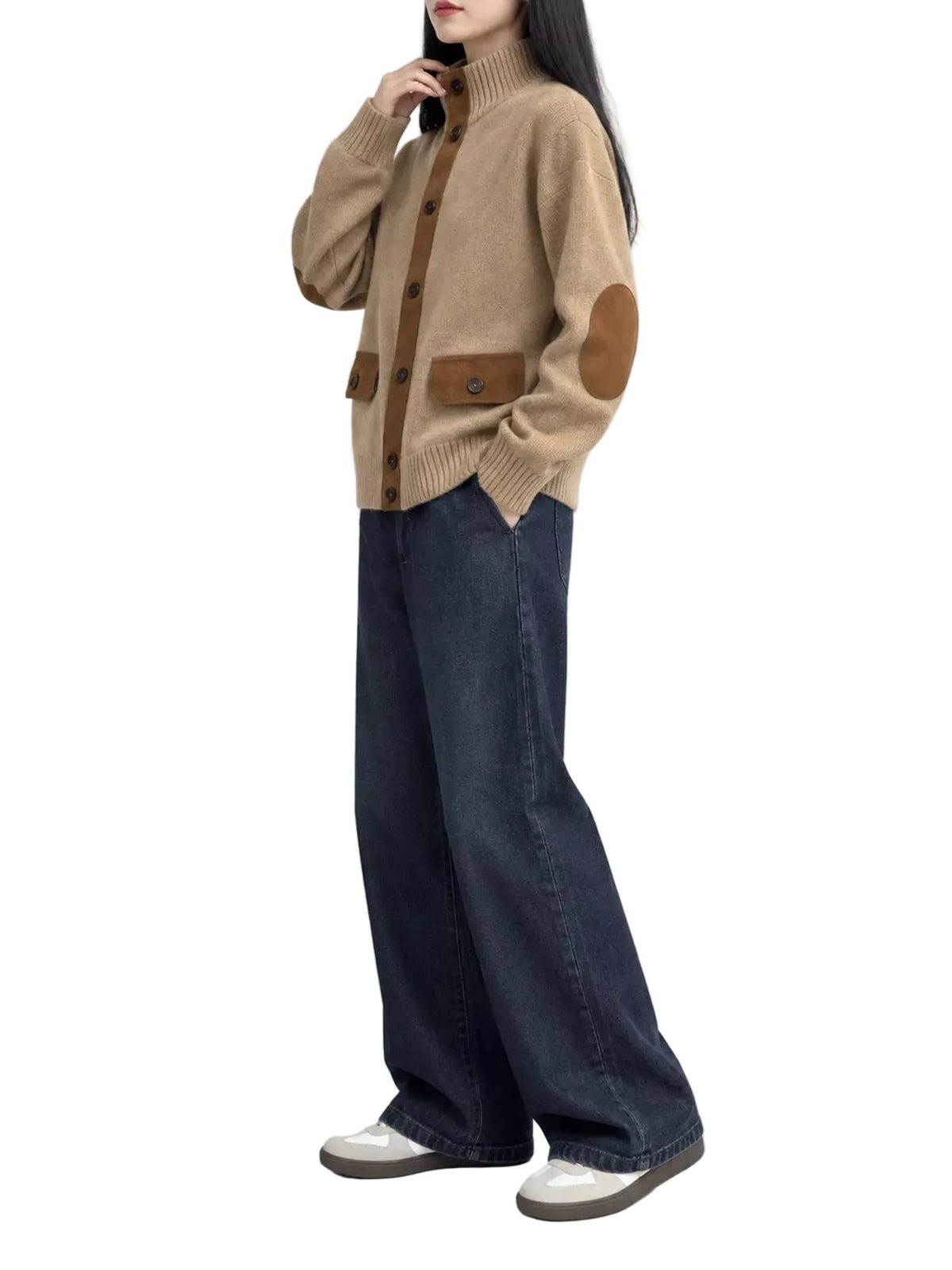 A model wearing a beige ribbed knit cardigan with brown patchwork elbow patches and button details, paired with dark wide-leg jeans and white shoes, set against a plain white studio background.