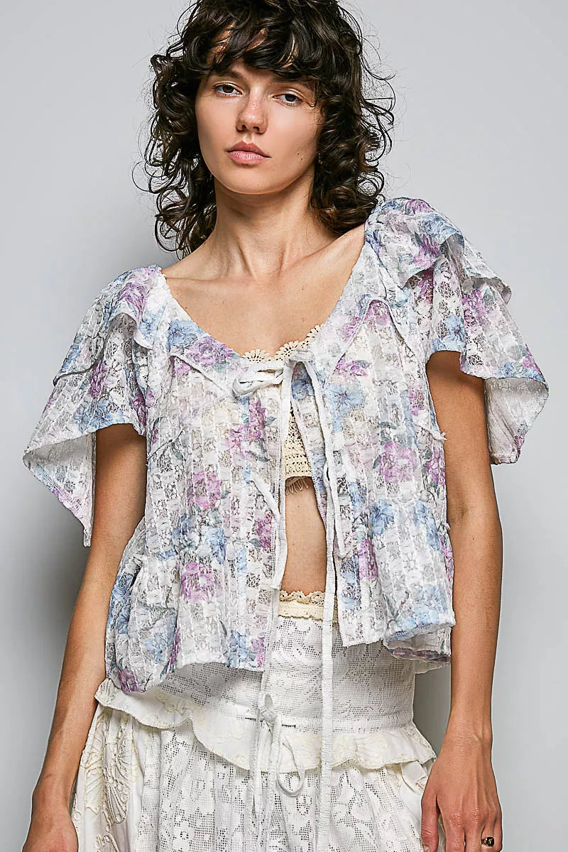 Woman wearing a floral blouse with ruffled sleeves against a plain background