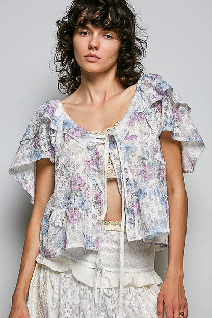 Woman wearing a floral blouse with ruffled sleeves against a plain background