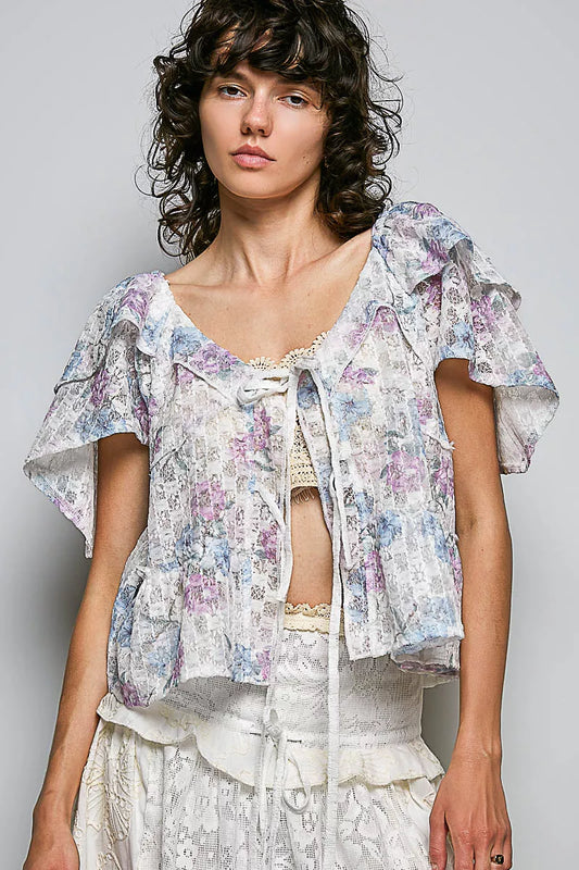 Woman wearing a floral blouse with ruffled sleeves against a plain background