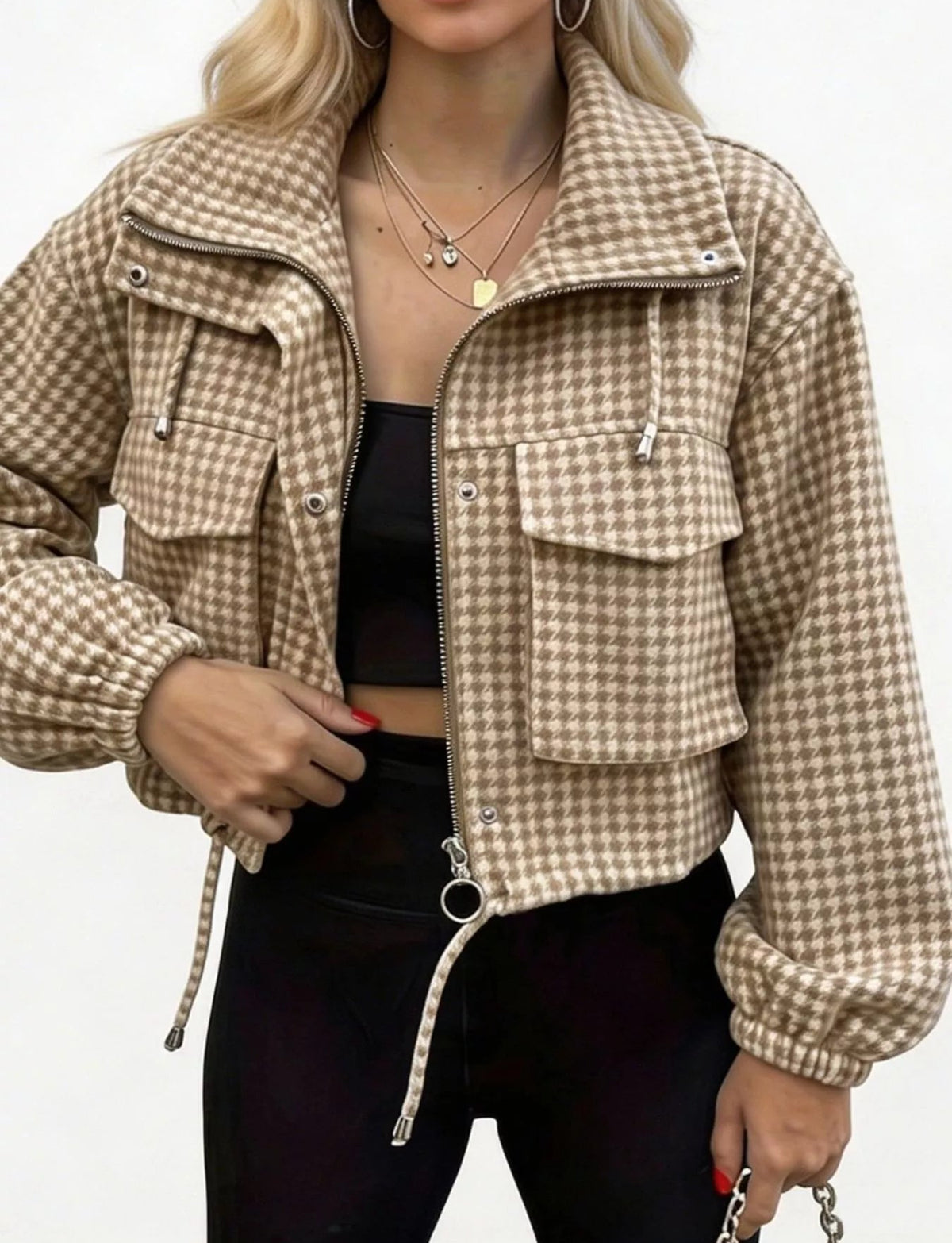 A woman wearing a cropped beige and brown checkered zip-up jacket over a black top and black pants, shown from the shoulders to the upper thighs against a plain light background.