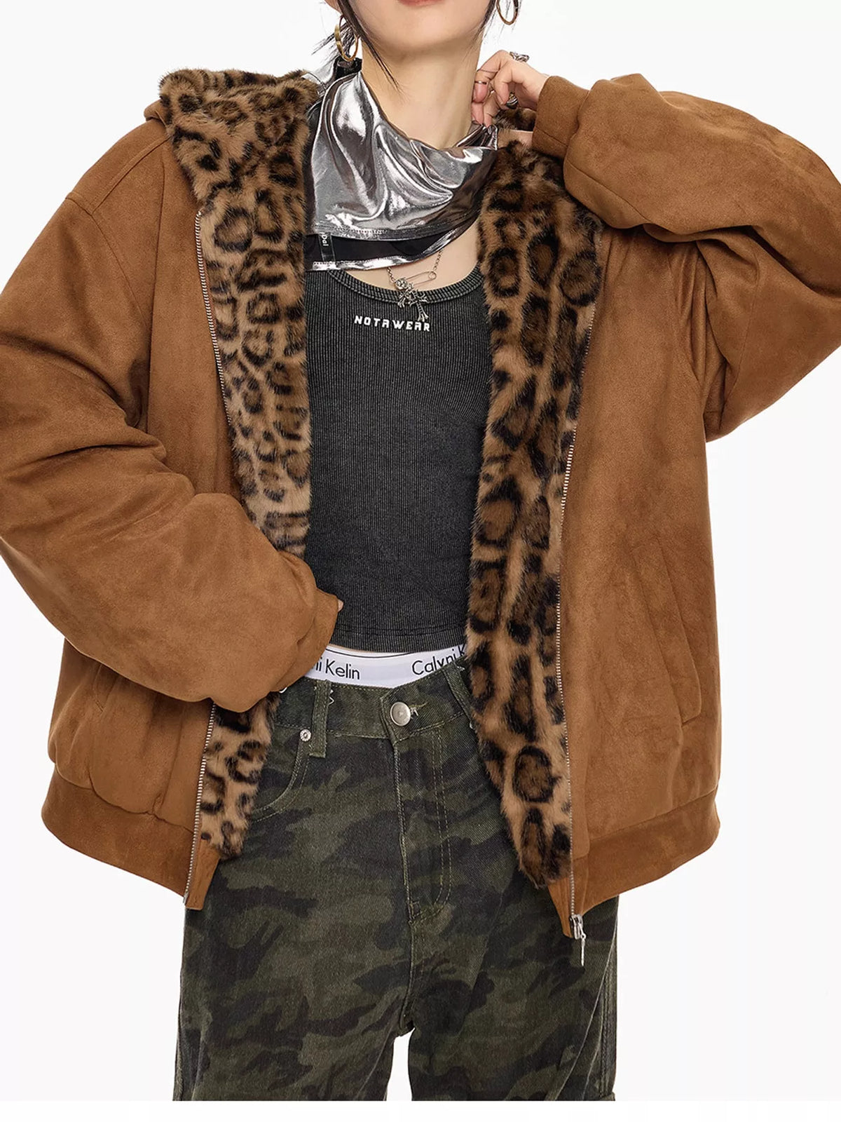 A person wearing an oversized brown suede-like jacket with a leopard-print faux-fur lined hood and collar, layered over a black top and camouflage pants against a plain light background.