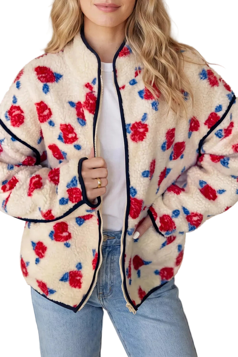 A woman wearing a cream sherpa jacket with a red and blue floral pattern and black trim, paired with a white top and light blue jeans.