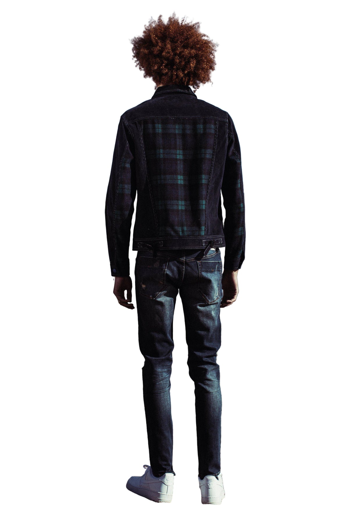 Person wearing a plaid shirt and jeans standing on a lakeside with mountains in the background