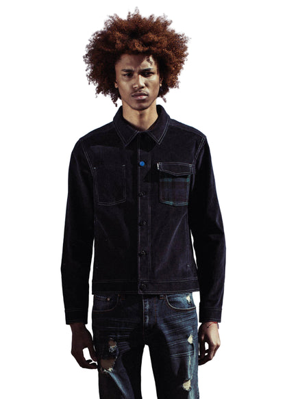 Person wearing a black jacket and jeans standing by a body of water with mountains in the background