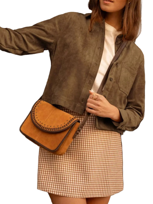 A woman wearing a brown suede cropped jacket, a brown and white gingham mini skirt, and a white top, carrying a brown suede crescent-shaped crossbody bag with a dark strap.