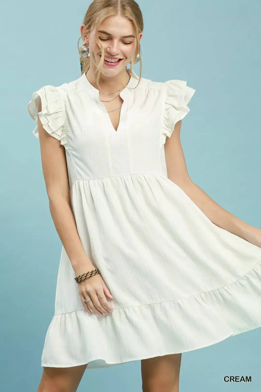 Woman wearing a white dress with ruffled sleeves against a light blue background