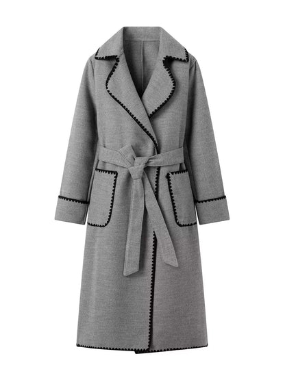 A gray wrap coat with black contrast stitching along the edges, featuring a tie belt, large front patch pockets, and a wide collar, shown against a plain white background.