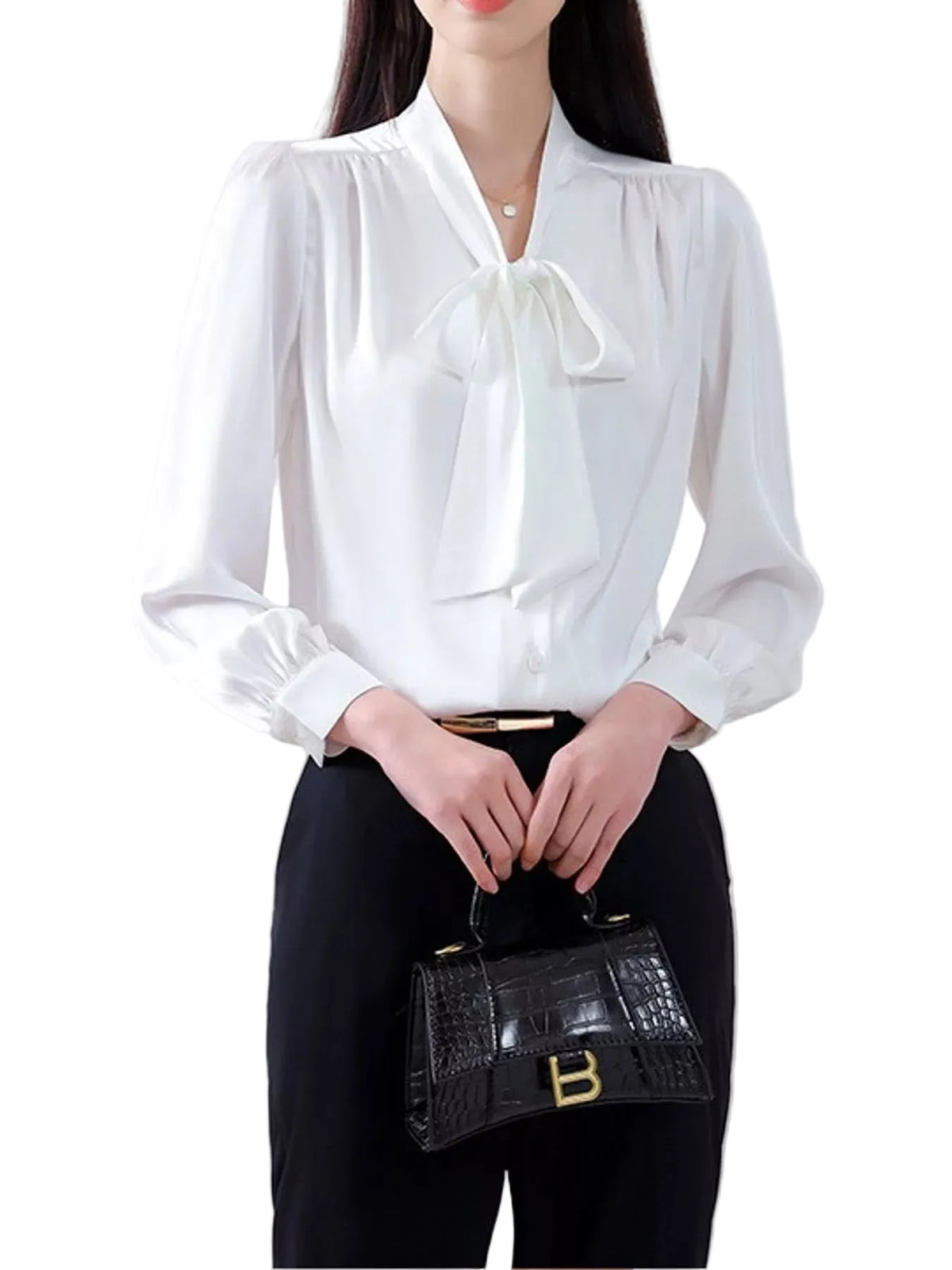 A woman wearing a white long-sleeve blouse with a large front bow and black pants, holding a small black crocodile-embossed handbag with gold hardware.