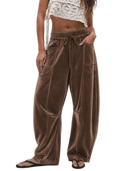 A model wearing brown wide-leg velvet pants with an elastic drawstring waist and side cargo pockets, paired with a white crochet crop top and black flip-flops against a light gray background.