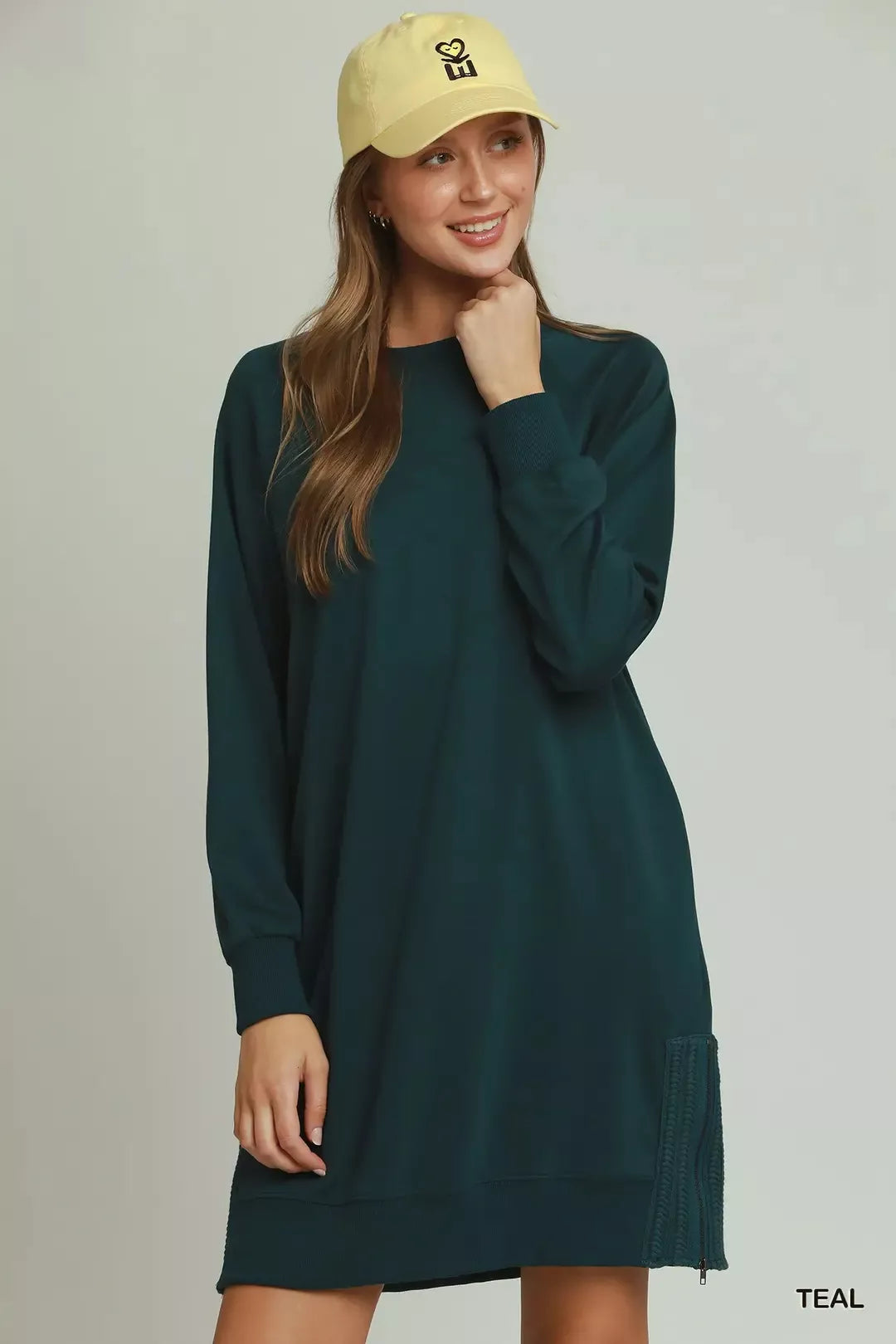 Woman wearing a teal dress and yellow cap on a plain background