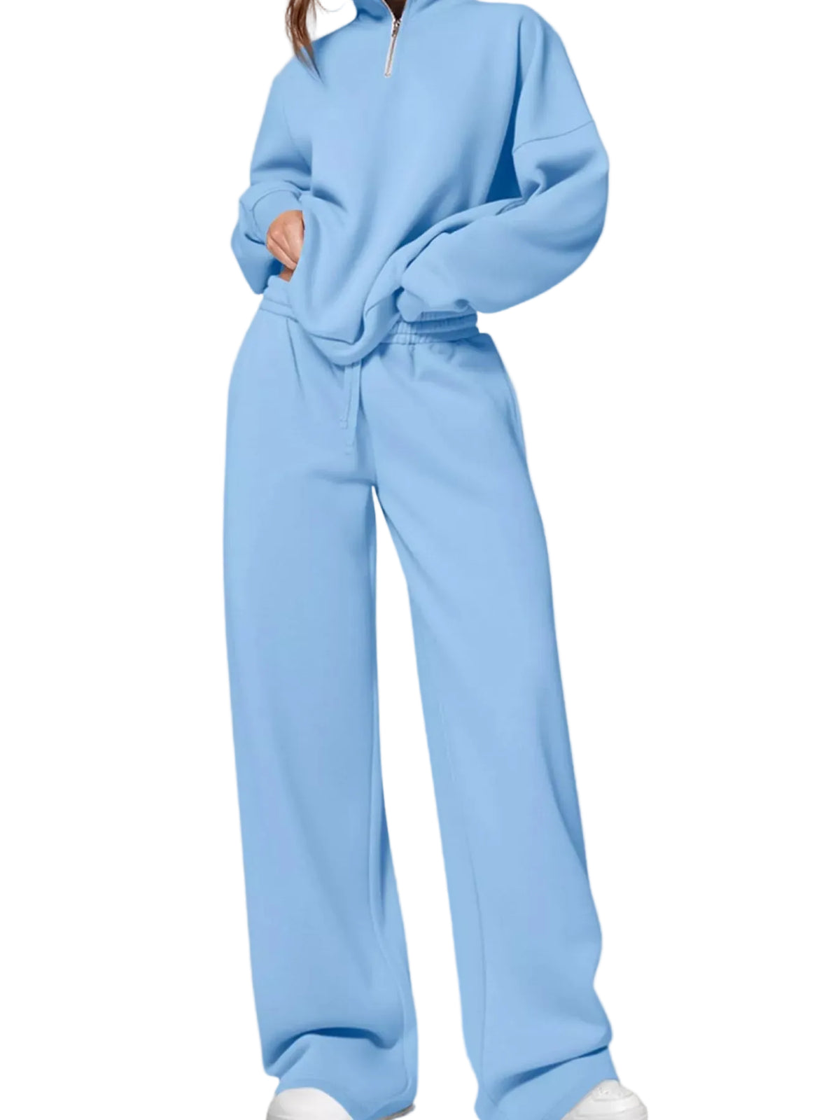 A person wearing a light blue matching lounge set consisting of a half-zip sweatshirt and wide-leg sweatpants, photographed against a plain light beige studio background.