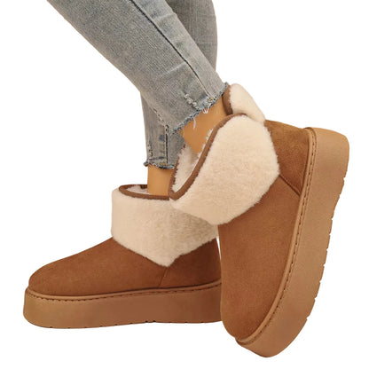 A pair of women's brown suede-like ankle boots with thick cream sherpa lining and platform soles, shown on a model wearing light-wash jeans against a textured beige wall.