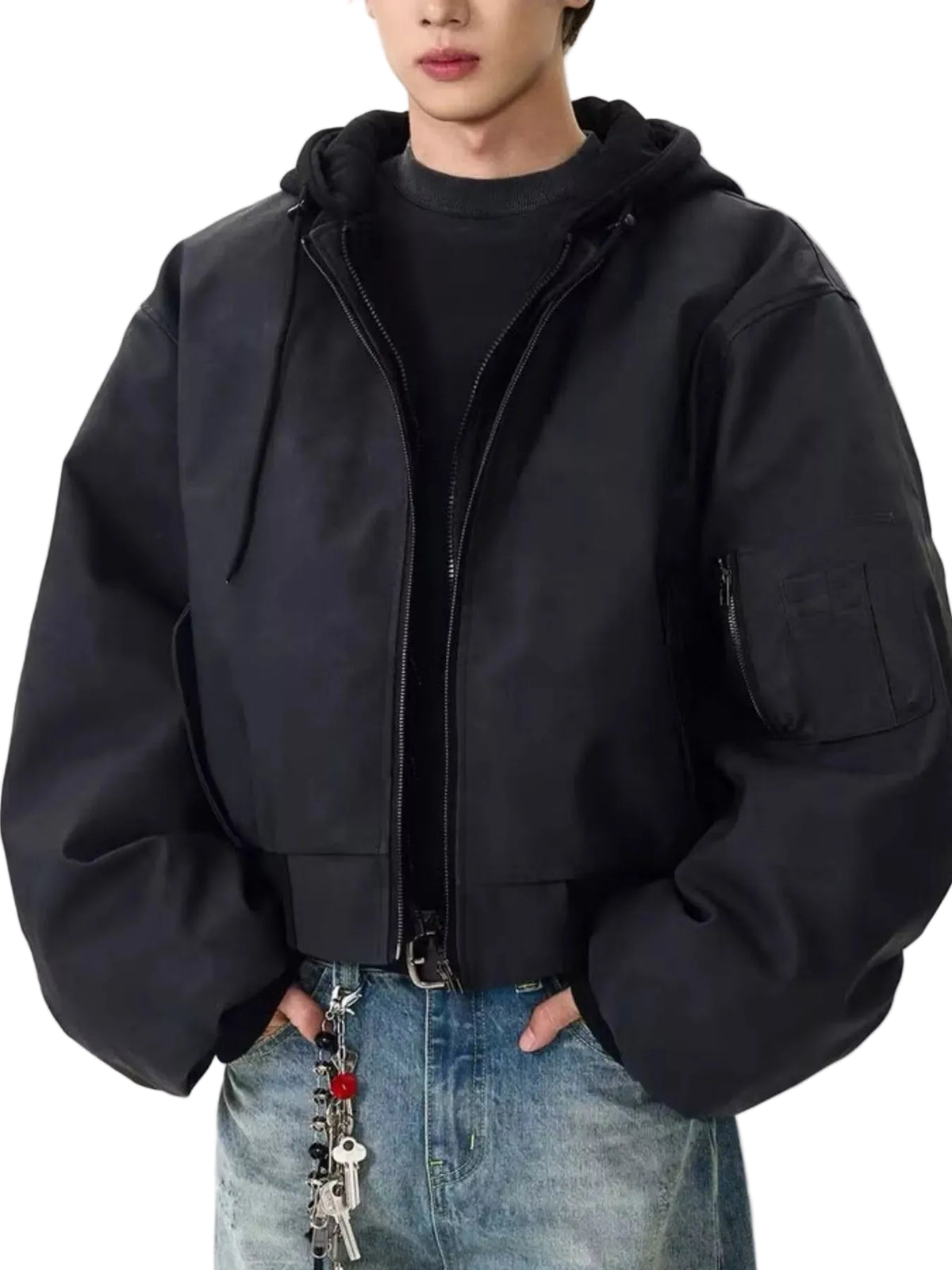 A person wearing a black oversized zip-front hooded jacket with a chest pocket, layered over a black top and blue jeans, against a plain light background.