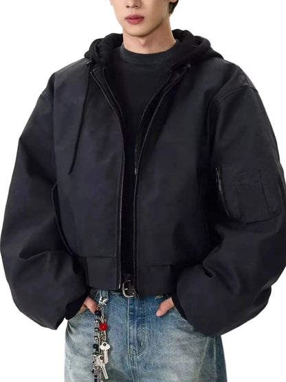 A person wearing a black oversized zip-front hooded jacket with a chest pocket, layered over a black top and blue jeans, against a plain light background.
