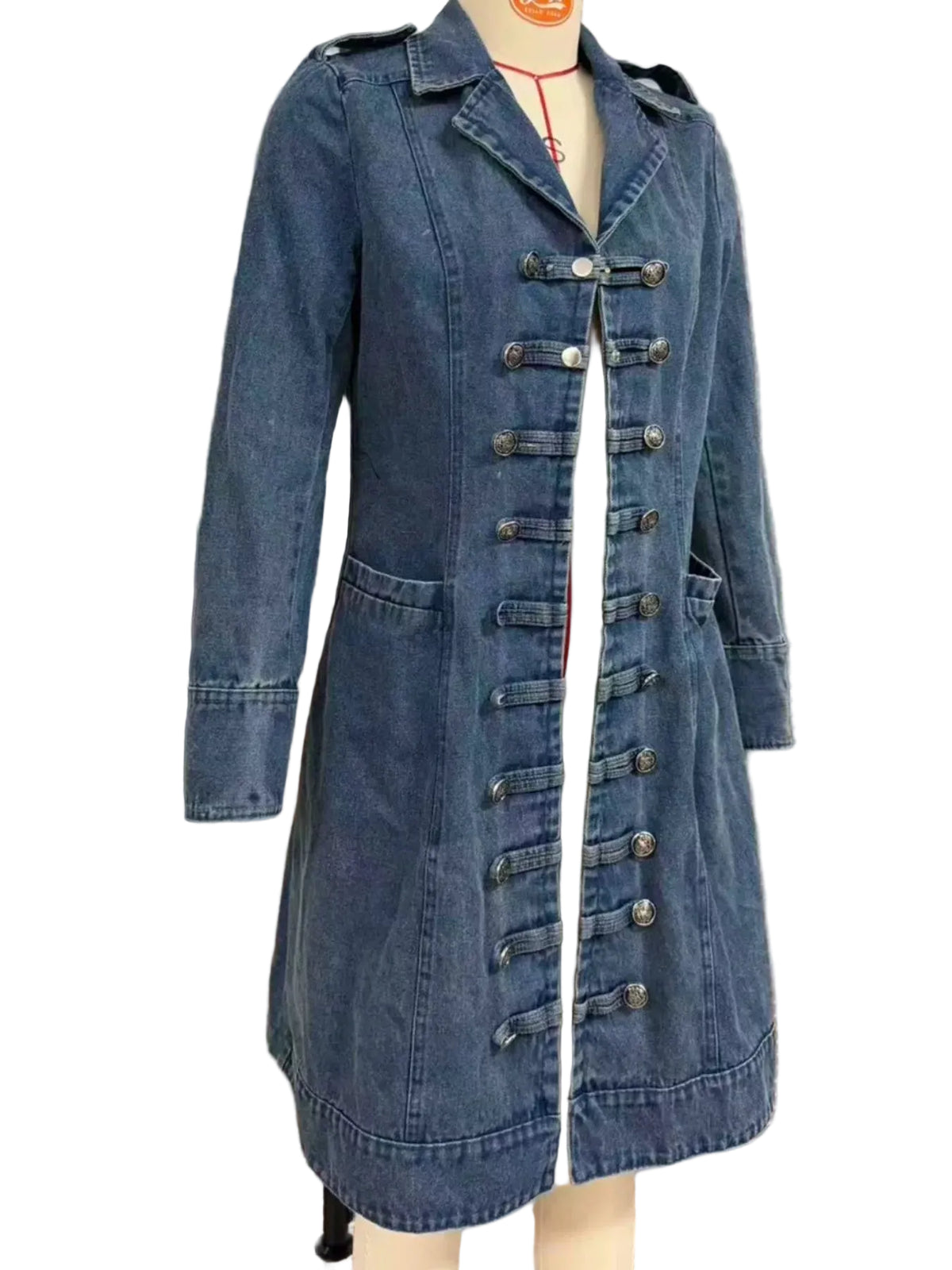 A blue denim trench coat with unique toggle-button closures down the front, displayed on a mannequin in front of a glass door with blinds.