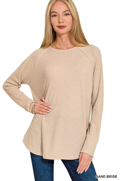 Woman wearing a sand beige long-sleeve top with blue jeans on a white background