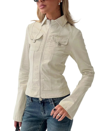 A woman wearing a fitted cream-colored zip-front jacket with flap chest pockets and blue jeans, photographed indoors against a light wall with a metal railing visible behind her.