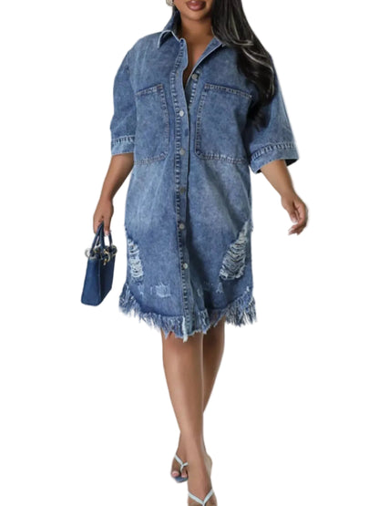 A woman models a distressed blue denim shirt dress with rolled sleeves and a frayed hem, holding a matching blue handbag against a light gray studio background.