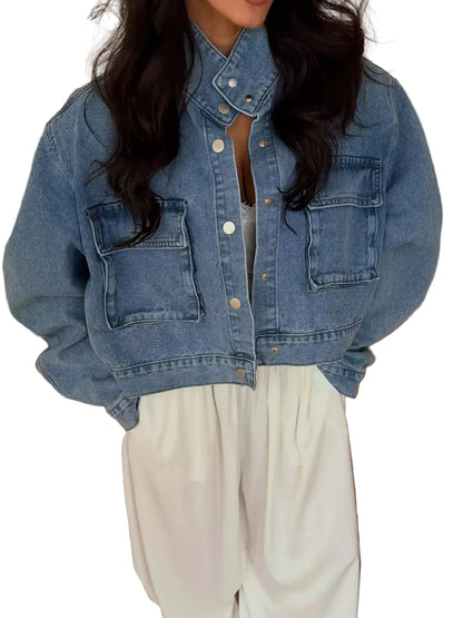 A person wearing a cropped light blue denim jacket with front flap pockets and white wide-leg pants, standing indoors on a wood floor.