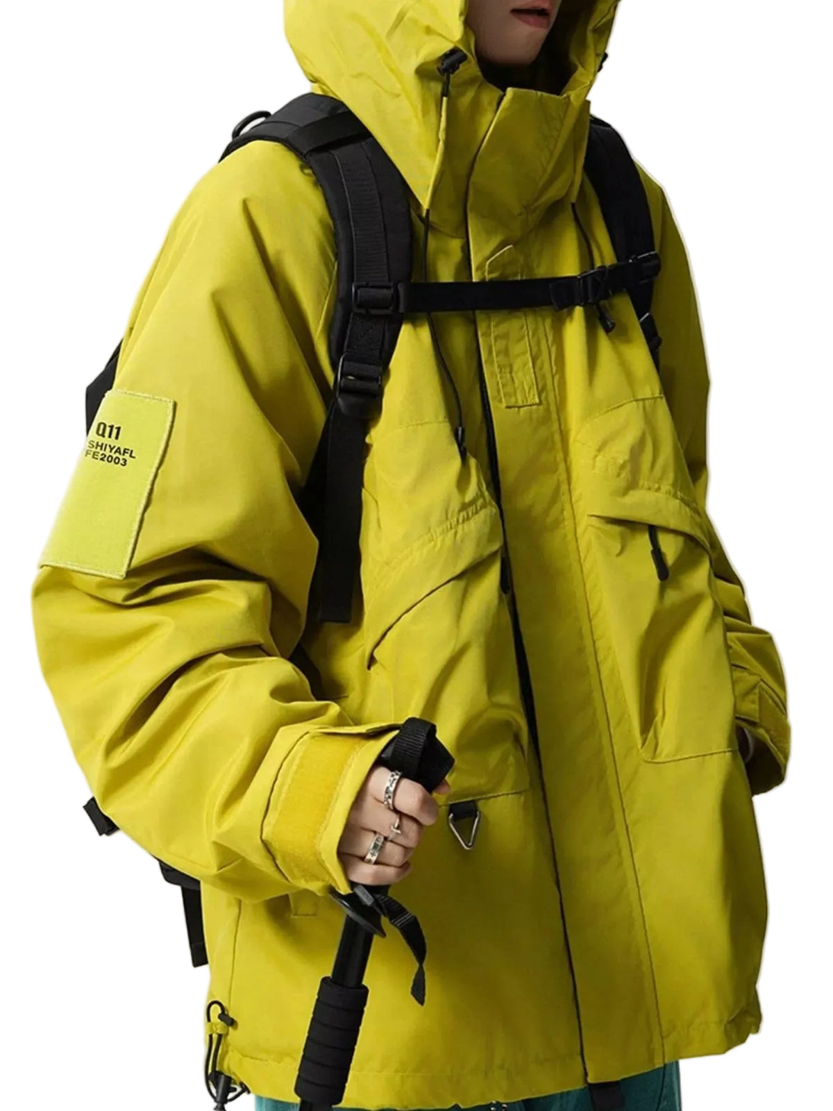 A person wearing a bright yellow hooded technical jacket with black backpack straps and a black handled pole visible, photographed against a plain light gray studio background.
