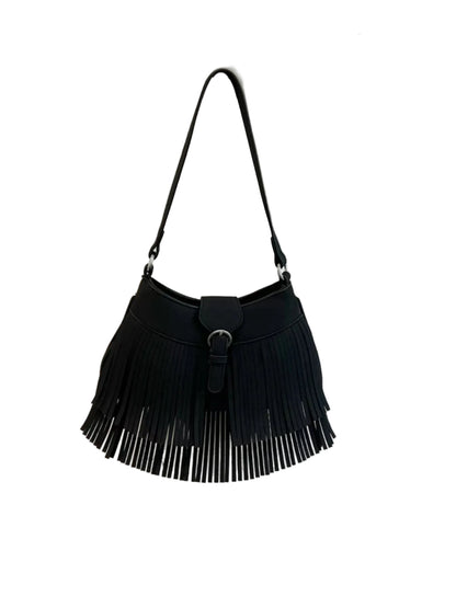 A black fringe shoulder bag hanging on a textured white wall next to a beige curtain, with a sign in the background that reads 'etc.' and 'ents anyway.