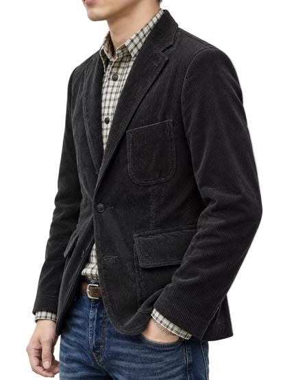 A man wearing a black corduroy blazer over a beige and black checkered shirt, paired with blue jeans, shown from the chest down against a plain white background.