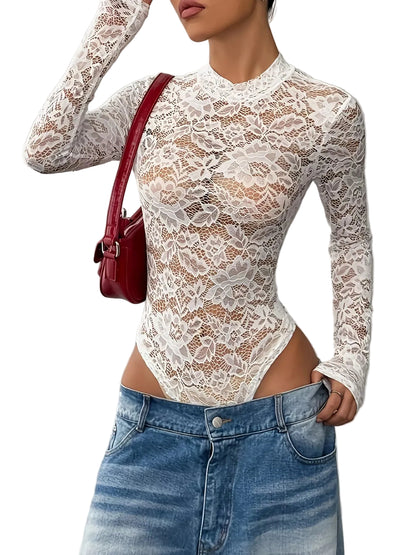 A woman wearing a white long-sleeve lace bodysuit with a high mock neck, paired with blue denim shorts and a red shoulder bag, shown against a gray wall.
