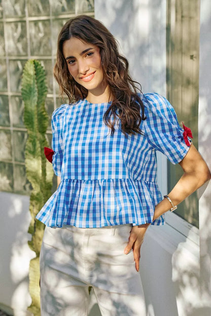 Woman wearing a blue checkered top with puffed sleeves in an outdoor setting.