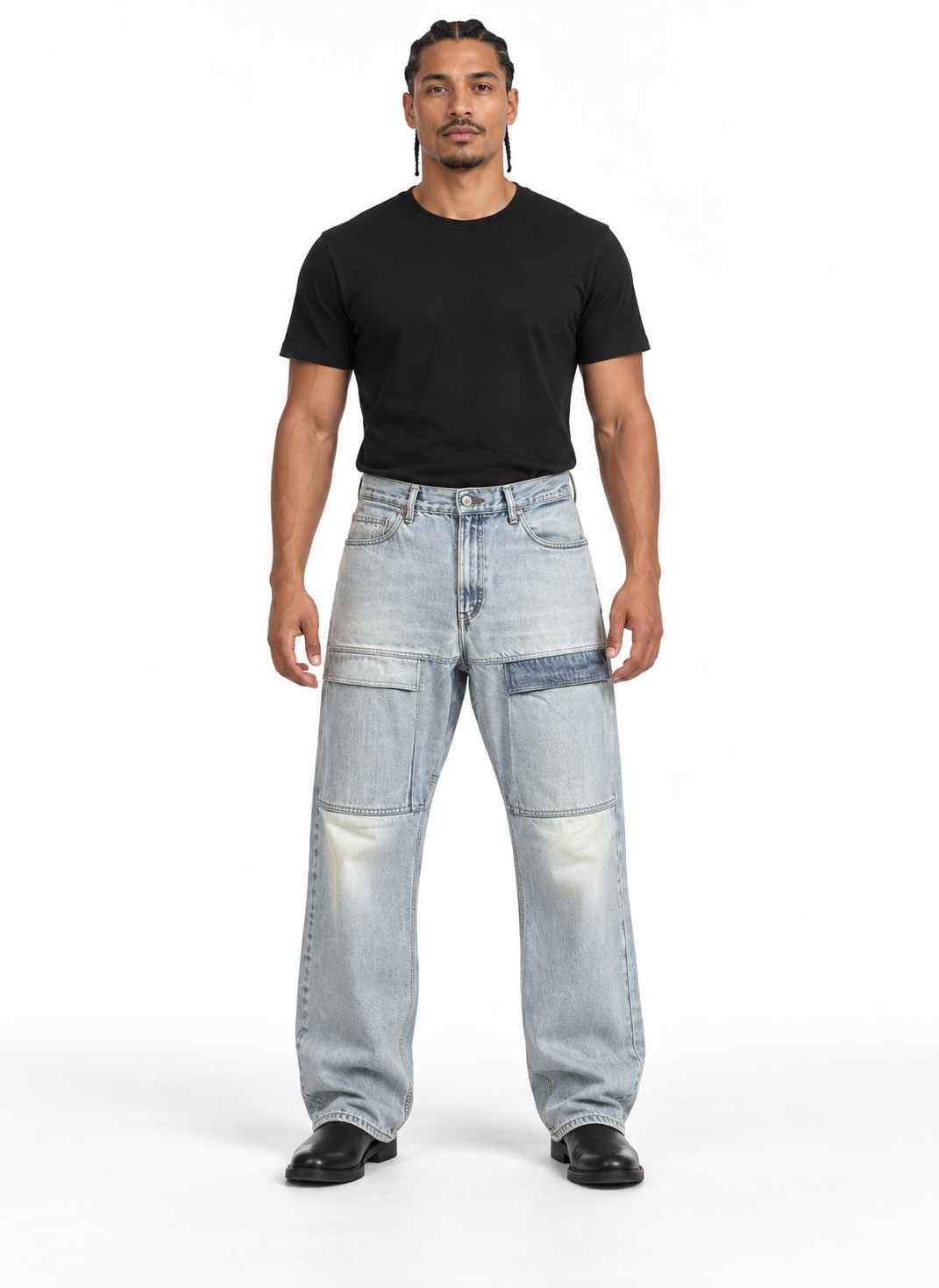 A man modeling a pair of light-wash, wide-leg patchwork jeans with a black t-shirt and black shoes, standing against a plain white studio background.